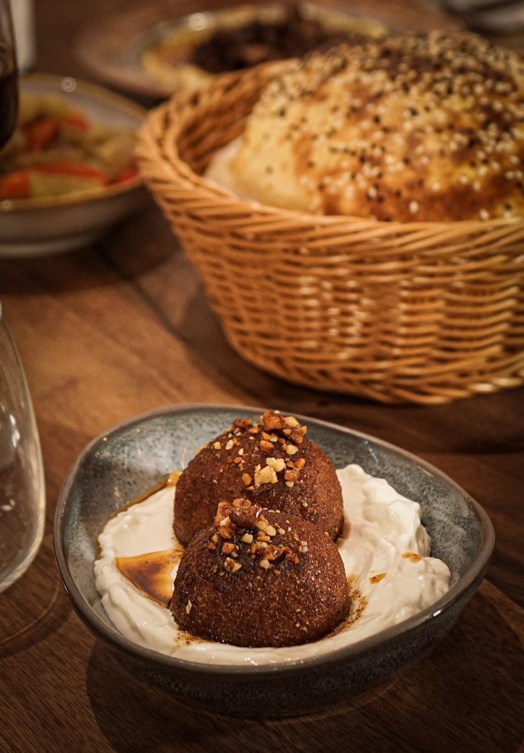 Two crisp kibbeh on whipped yoghurt, with a basket of sesame-topped bread