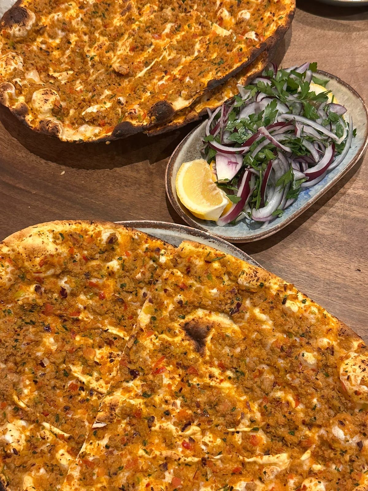 Two charred lahmacun beside a plate of red onion and parsley salad with lemon
