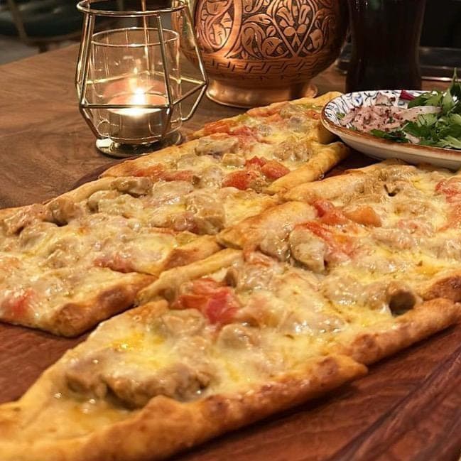 Cheese and lamb pide on a wooden board, a candle glowing beside it